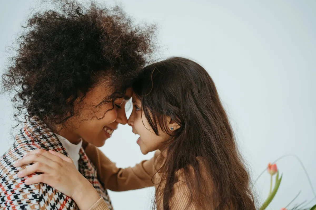 A mother and her young child touch foreheads and smile at each other.