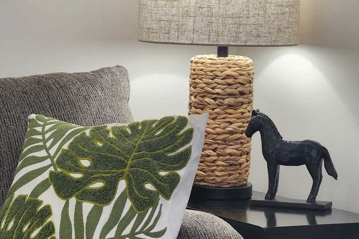A cozy seating corner in the Raleigh office — a soft gray sofa with a green palm-leaf pillow beside a woven table lamp.