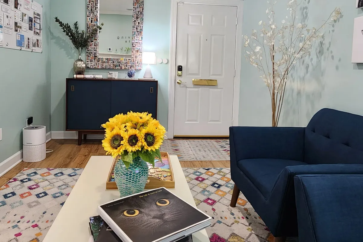 The Raleigh office entrance and waiting area — sage-green walls, navy armchairs, a bright bouquet of sunflowers on the coffee table, and a patterned rug.